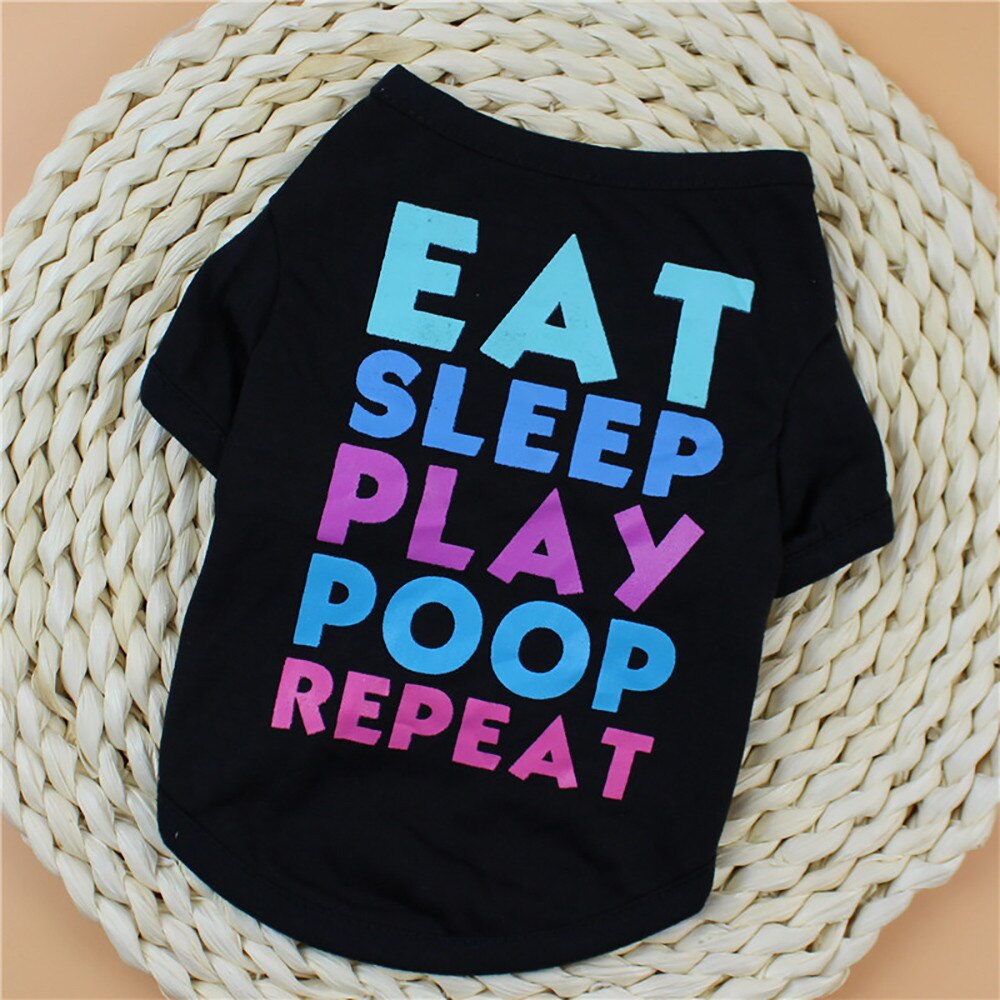 Black Eat Sleep Play Poop Repeat pet shirt laid diagonally on a woven mat