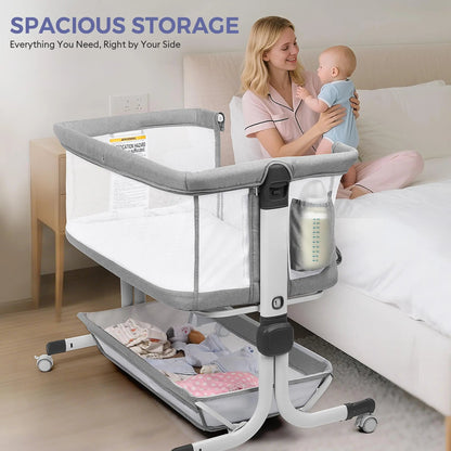 Mother holding a baby beside a gray bassinet with a side pocket and lower storage shelf.