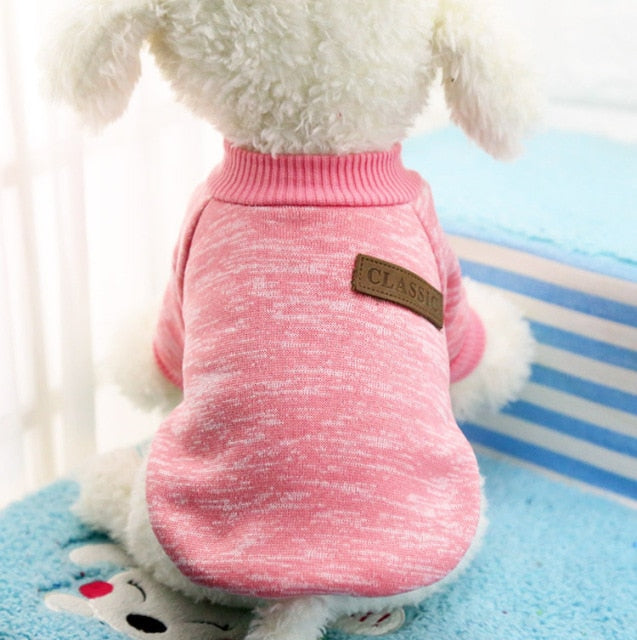 Pink pullover pet sweater with ribbed trim and a decorative back patch on a white plush dog