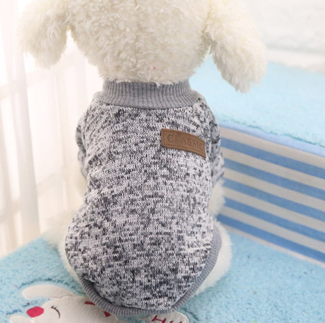 Grey marled pullover pet sweater with ribbed trim and a decorative back patch on a white plush dog